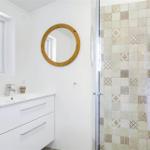 Badezimmer mit Dusche, Waschbecken und runden Spiegel