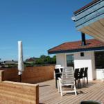 Terrasse mit Holzdecke, Tisch, Stühlen und Schutzdach. Hintergrund: Haus und Bäume.