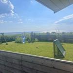 Grüner Garten mit Spielplatz und Meerblick. Holzzaun und blaue Rutsche sind sichtbar.