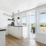 Küche mit Blick auf den Strand und Terrasse. Weiße Schränke, Holzboden und Fensterfront.