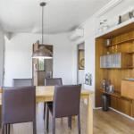 Esszimmer mit Holztisch, vier Stühlen und Holzwandregal. Deckenleuchte und Fenster sichtbar.