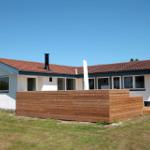 Wohnhaus mit Holzterrasse und rotem Dach unter blauem Himmel.