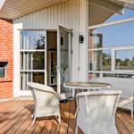Deck with table and chairs, glass facade and brick wall. Door leads inside.