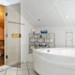 Bath with whirlpool and adjacent sauna. Shelf with baskets and model boat.