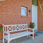 A white bench stands before a red brick wall beside a door with house number 8.