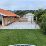 House with terrace, paved yard, and garden. White shed and green trees are visible.