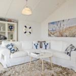 Living room with white sofa, beach artwork, and bookshelf against wall.