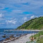 Dock, beach, and green cliff under blue sky.