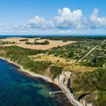 Aerial view of coastal village with cliffs, fields, and houses near the sea.