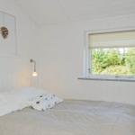 A bedroom with white wood paneling, a bed, and a window with a view of trees.