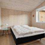 Schlafzimmer mit Holzwandverkleidung, Bett und Fenster mit Blick auf Wald.