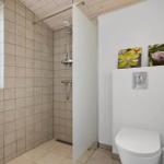 Bad mit Dusche, Toilette und Waschbecken. Fenster, Wandbild und Holzdecke.