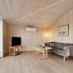 Wohnzimmer mit Holzwand, Sofa, Tisch und TV. Große Fenster mit Blick nach draußen.