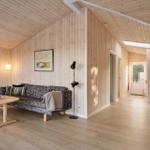 Wohnzimmer mit Holzwand, Sofa, Tisch und Stehlampe. Durchgang zu einem weiteren Raum.