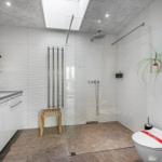 Badezimmer mit Dusche, Waschbecken und Toilette. Glaswand, Pflanzen und Wandbild.