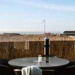 Terrasse mit Tisch und Stühlen, Blick auf Feld und Meer.