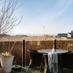 Terrasse mit Tisch, Stühlen und Blick auf Feld und Meer.