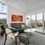 Wohnzimmer mit Ledersofa, Sessel und runden Teppich. Große Fenster und Glasschiebetüren.