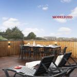 Terrasse mit Tisch, Stühlen und Liegestühlen. Holzgeländer und Blick auf Grünflächen.