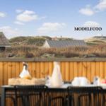 Terrasse mit Tisch und Stühlen. Hintergrund: Dünengrund mit Häusern und blauem Himmel.