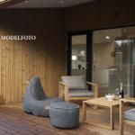 Terrasse mit Sitzgruppe und Blick ins Haus. Holzwand und Glasfront.