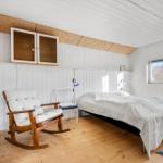 Schlafzimmer mit Bett, Schaukelstuhl und Holzboden. Weiße Wände und Decke.