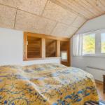 Schlafzimmer mit Bett, Holzdecke und Fenster mit Blick auf Bäume.
