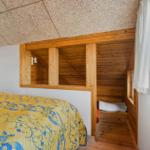 Schlafzimmer mit Holzbett und Fenster. Decke aus Holzspanplatten.