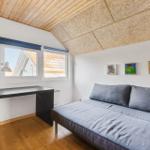 Zimmer mit Schlafcouch, Schreibtisch und Fenstern. Holzdecke und Wandbilder.
