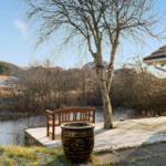 Terrasse mit Holzbank und Baum neben Haus, Blick auf Fluss und Hügel.