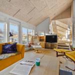 Wohnraum mit gelbem Sofa, Kamin und großen Fenstern zur Aussicht.