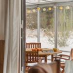 Terrace with wooden table, chairs, and snow outside. Hanging string lights and oranges on the table.