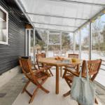 Patio with wooden table and chairs, snow outside, string lights on the ceiling.