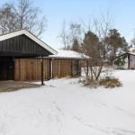 Snow-covered garden with wooden garage and holiday house in the woods.