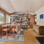 Dining area with wooden table, bookshelf, and wood-burning stove. Wooden walls and parquet floor.