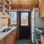 Kitchen with wood walls, refrigerator, stove, and window to outside door.