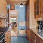 Kitchen with wooden furniture, coffee maker, and kettle. Corridor to living room with chair.