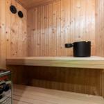 Sauna with wooden walls, bench, and black bucket.