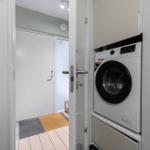 Washing machine in a narrow room next to a door with tiled floor.