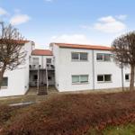 White vacation apartment with red roof, balcony, and stairs to the entrance door.