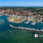 Aerial view of harbor town with marina, boats, and red-roofed houses near sea.