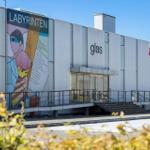 Modern glass gallery with large wall art and flag. Entrance with stairs and railing.