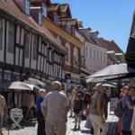 Street with half-timbered houses and pedestrians. Shops and stalls along the cobblestone path.
