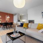 Living room with sofa, coffee table, and fireplace. Dining area with table and chairs. Kitchen area visible.