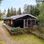 A dark wooden house with glass front and stone wall in the forest.