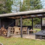 Outdoor area with seating, table and chairs under roof. Woodpile and grill area visible.