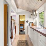 Kitchen with wooden floor, white cabinets, and view into bedroom with bunk bed.
