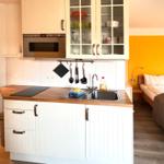 Küche mit weißen Schränken, Edelstahlspüle und integriertem Ofen. Im Hintergrund ein Bett.