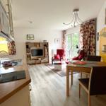 Küche, Essbereich und Wohnzimmer mit TV, Sitzgelegenheiten und Balkonzugang.