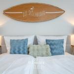 Schlafzimmer mit Bett, Kissen und Nachttischen mit Ankerlampen. Wanddekoration mit Surfbrett.
